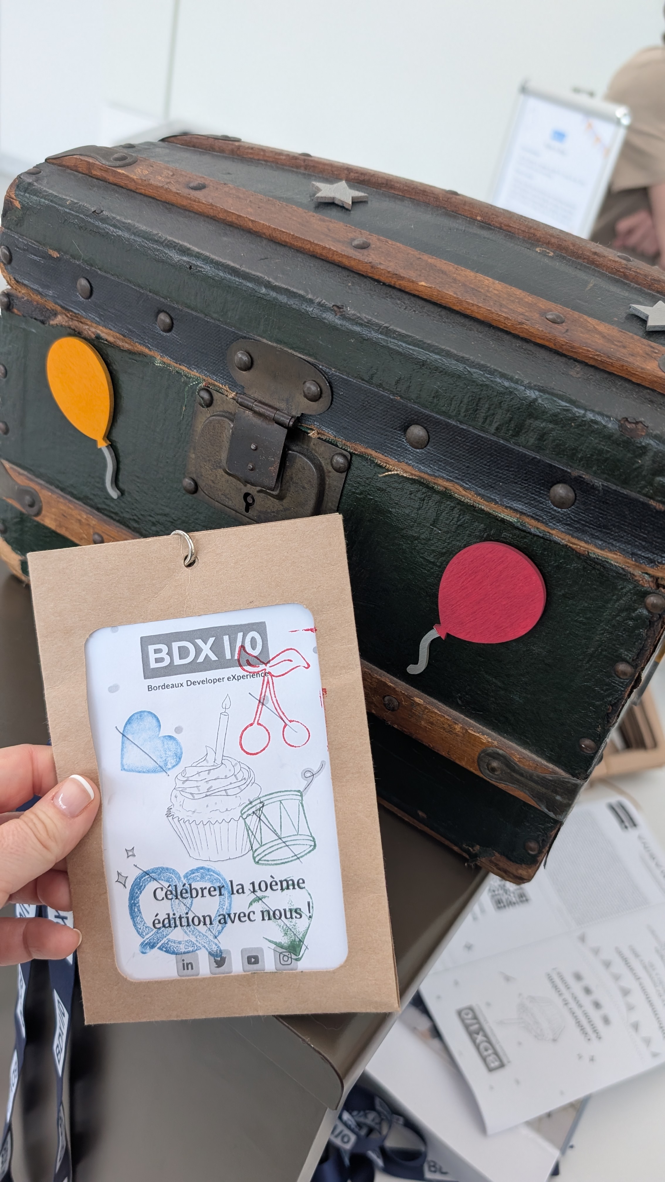 Photo du billet conférence tamponné plusieurs fois, tenu à la main devant un coffre au trésor