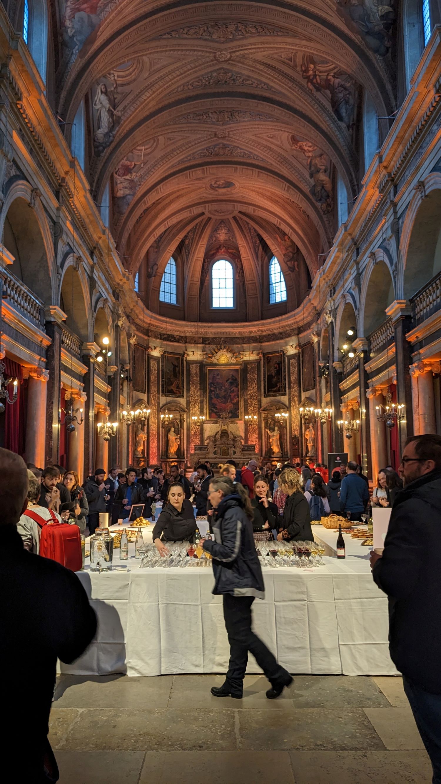 Photo de l&rsquo;intérieur de la Chapelle de la trinité, assez coloré et chaleureux, avec des tables accueillant le buffet, et des personnes tout autour.